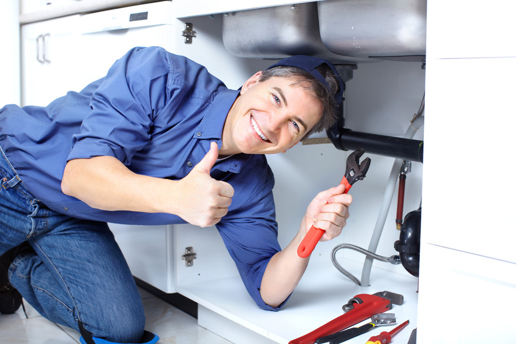 Mature plumber fixing a sink at kitchen